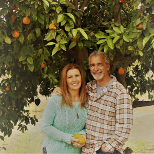 Couple showing a man and woman standing under a lemon tree with the woman holding some lemons